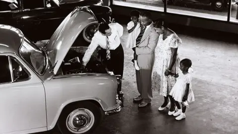 Getty Images A family in Guyana are shown a Morris car in a showroom, 1958.