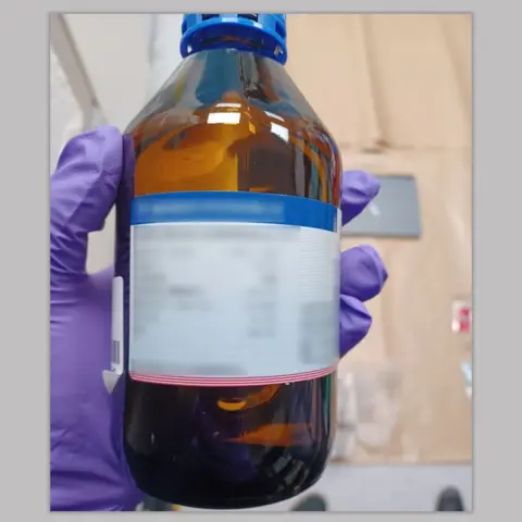 Metropolitan Police A hand in a purple rubber glove holds a brown bottle which police found inside Zou's flat