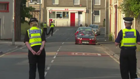 The backs of two police officers are seen, while in the distance are two more police officers