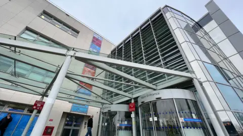 Stuart Woodward/BBC The entrance to Broomfield Hospital, a glass-fronted building with revolving doors. 