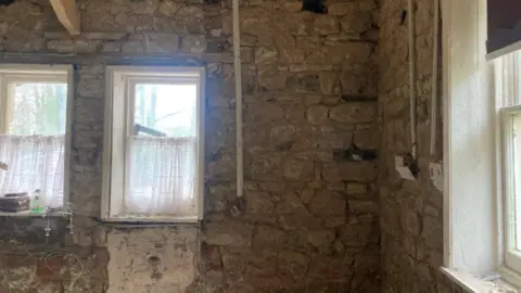 Girlguiding Cleveland A bare stone wall in the interior of a house - plugs banks are hanging out the wall, mould can be seen underneath a window.