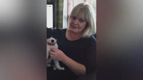 Louise Muldoon Louise with blonde hair and a blue top holding a dog