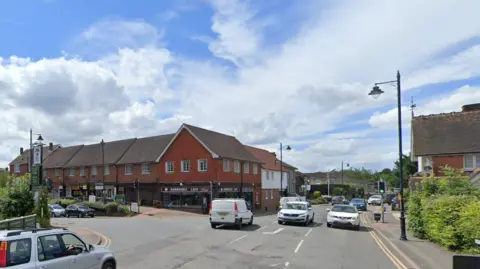 Google A Google StreetView of a busy intersection. There are lots of cars and red buildings line the roads