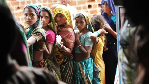 Getty Images MADHYA PRADESH, INDIA - JULY 2010: A group of Indian women line up outside the Fair Price Shop with their ration cards to receive portions of wheat, sugar, kerosene and rice in Jhabua state, Madhya Pradesh, India, in July. 16, 2010. T