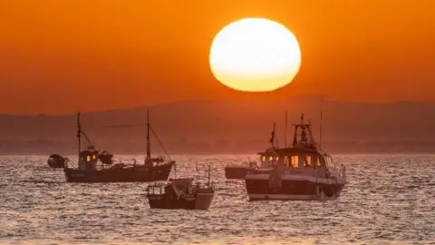 BBC Weather Watchers/Coastal JJ Boats on the water at sunrise with an orange sky and huge sun in Selsey, West Sussex