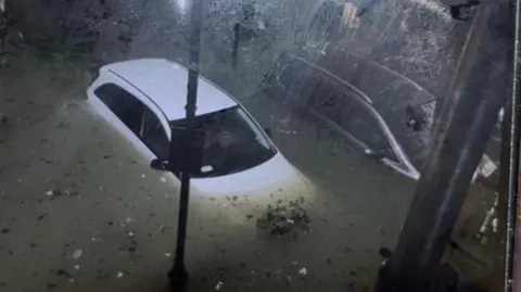 A white car is surrounded by water. The photo was taken at night from above. 