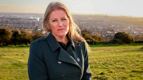 Donna Jones is standing in a grassy area with a city behind