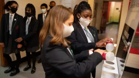 Getty Images Year eight pupils wearing face masks sanitise their hands in a corridor at Moor End Academy in Huddersfield, on September 11, 2020.
