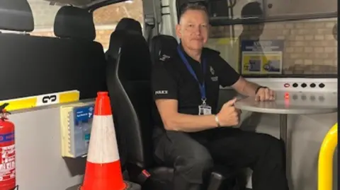 Wiltshire Police Sgt Hatch sitting inside a police van with a road traffic cone beside him