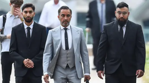 PA Media Human Rights lawyer Aamer Anwar (centre) arrives with Mohammed Fahir Amaaz (left) and Muhammed Amaad (right) at Liverpool Crown Court, where they are charged in relation to an altercation with police officers at Manchester Airport's Terminal Two on July 23 2024.