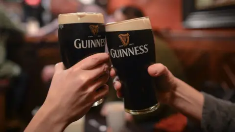 Two people toasting two pints of Guinness