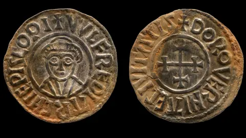 A silver ingot coin which has shows a man on one side and a cross on the other