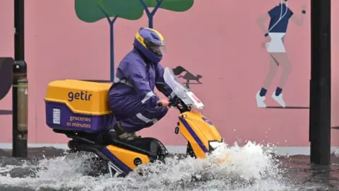 Getty Images A motorcyclist drives through deep water on a flooded road in The Nine Elms district of London