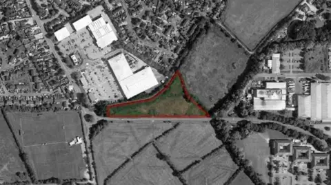 Drynham Lane Ltd An aerial view of the agricultural land in Trowbridge. There is a green elongated triangular patch in the middle, outlined with red, indicating where the development could be built. The rest of the image has been masked in black and white.