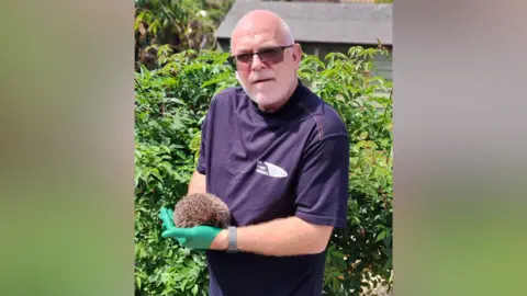 UK Power Networks Jon Gray is wearing green gloves and holds a hedgehog