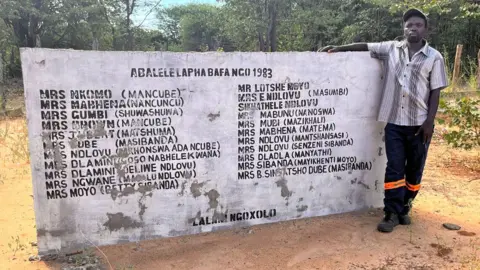 BBC Thabani Dhlamini by a memorial wall to those who were killed in his village of Salankomo by Zimbabwean soldiers in 1983