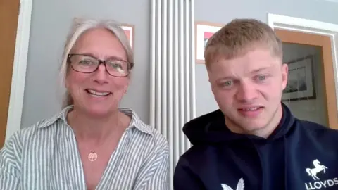 A mum with grey hair and her son with blonde hair smile at the camera via zoom.