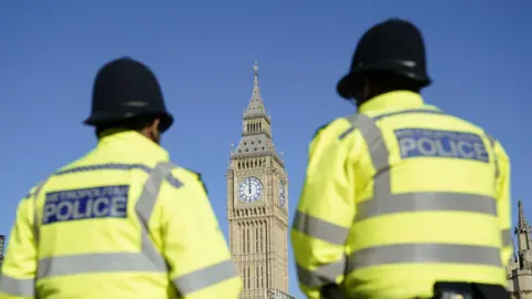 PA Media File image the Elizabeth Tower, part of the Palace of Westminster, seen between two out-of-focus uniformed Metropolitan Police officers in Parliament Square