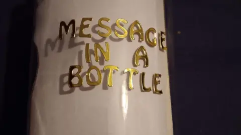 Close up of bottle with the words Message in a Bottle written on it in gold letters