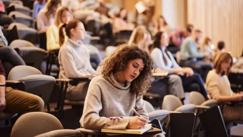 Getty Images A group of students in a lecture theatre, sat down making notes
