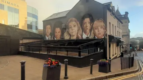 BBC Derry Girls mural showing the characters on a gable wall with awning blocking the view of the bottom half