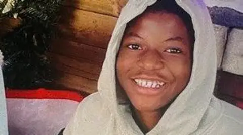 A boy wearing a grey hoodie while smiling at the camera.