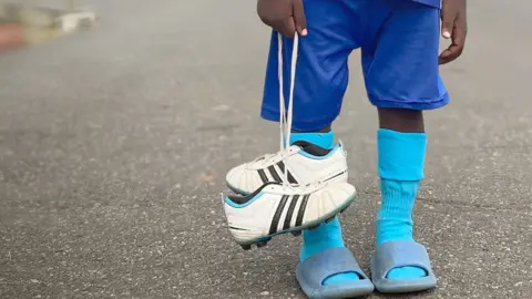 BBC A young boy holding football shoes in Gabon