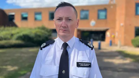 Nicola Haseler/BBC Assistant Chief Constable John Murphy, with short hair and a grave expression, wearing police uniform standing in front of the police HQ in Kempston.