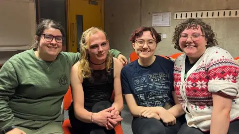 BBC/ Emily Johnson Four Morris dancers sit on orange chairs and look straight into the camera 