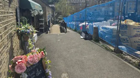 Hayley Coyle/BBC A picture of the exterior of Hobsons Florist with a blackboard outside overlooking a car park full of debris and building machinery.