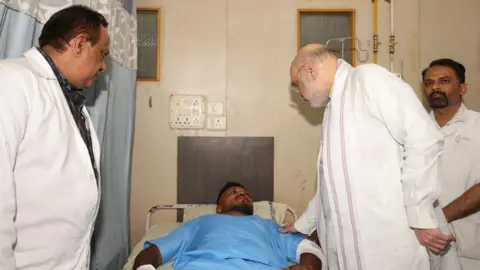 Vishwashkumar Ramesh lying in hospital bed as he is visited by India of Home Affairs Minister Amit Shah