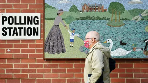 Map in a mask walking passed a polling station sign