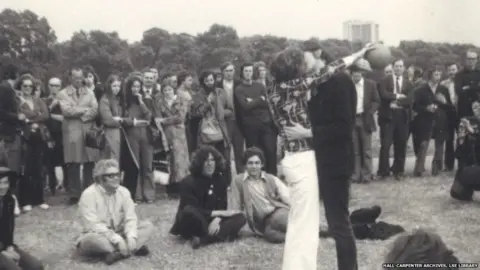 Hall-Carpenter Archives, LSE Library Black and white photograph of two men kissing in a park while a group watch on