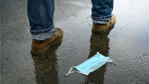 Getty Images A man walks by a discarded face mask lying in a puddle