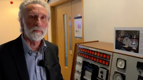 Trevor Chambers, the former head of the reactor centre, stands next to the original control panel
