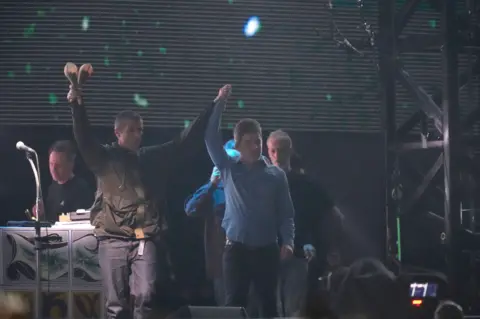 PA Media Liam and Noel Gallagher raise their hands in celebration during a show at their 2025 reunion tour