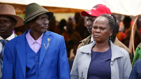 Peter Njoroge / BBC Dos adultos elegantemente vestidos, un hombre y una mujer, en el funeral. 