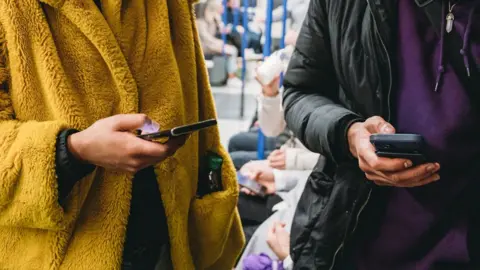 Getty Images Viajantes usam seus celulares em um trem