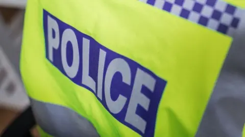A close-up of the back of a police officer's hi-vis jacket. It says "police" in large white letters inside a blue square.