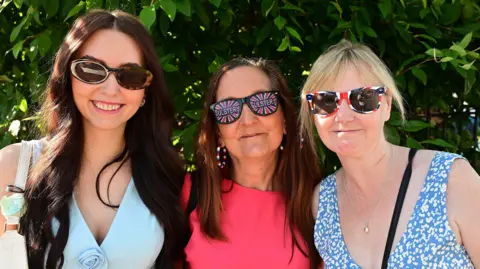 Pacemaker Three women smiling at the camera. They are wearing Union flag glasses and summer clothes.