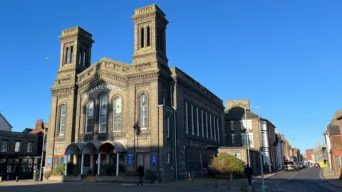 Andrew Turner/BBC Christchurch church in Great Yarmouth, a large brick building with a gabled end and large windows. Two brick towers adorn the building. There is a blue sky behind it.