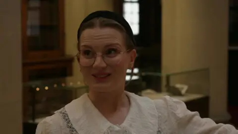 Dr Eleanor de Spretter Young, who wears glasses and a white blouse, explains the history of the Birds of America in Liverpool Central Library