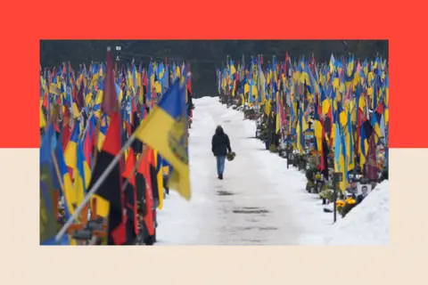 A person walks down a memorial, with flowers in their hand, in Lviv