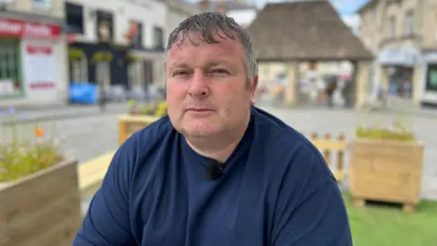 BBC A man in a blue t-shirt siting on a bench in Chippenham town centre