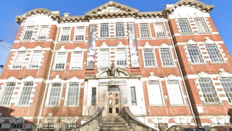 Google A street view of the outside of Exeter Phoenix. It is a three story building with tall windows and red brick. There are steps up.