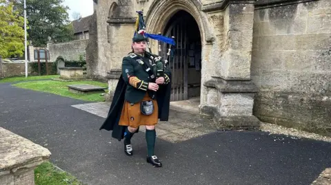 A bagpiper playing in military regalia outside an old church entrance. 