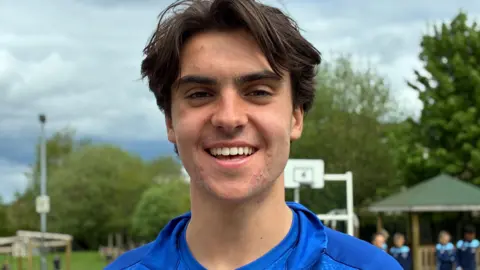 A boy with long brown hair wears a blue football shirt.