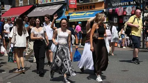 A crowd of young people on a pedestrianised shopping street, wearing summery clothes on a sunny day.