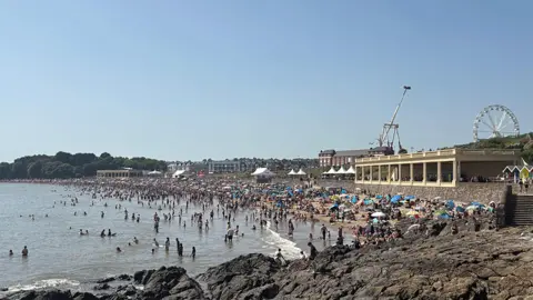 Barry Island beach is packed with beach-goers and you can see the Barry Island pleasure park in the background. 