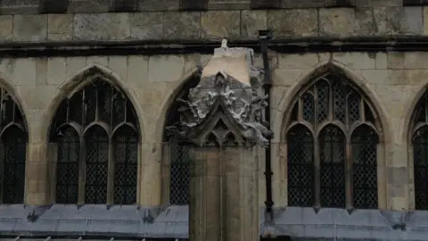 A broken stone finial on the roof of Hull Minster. Five arched windows are visible in the background.